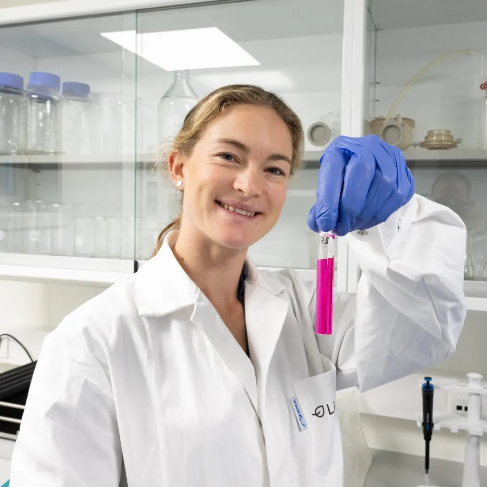 Kvinnelig forsker holder opp reagensrør med rosa væske i laboratorium